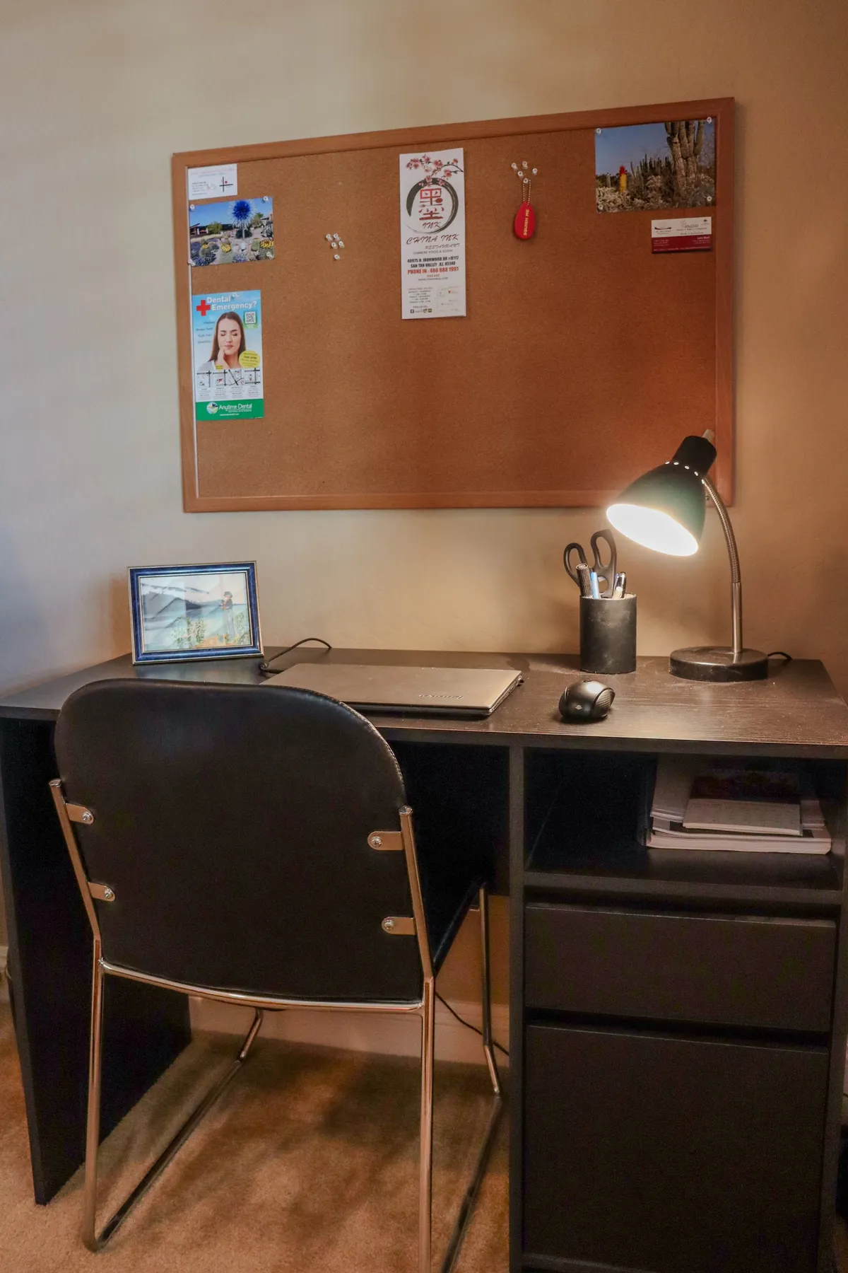 A focused workspace setup with a corkboard filled with notes, a desk lamp, computer, mouse, and framed picture. The area exudes a calm and productive environment, ideal for remote work or study.