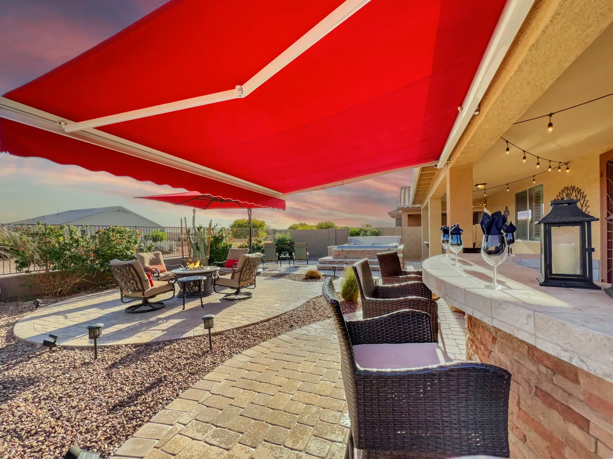 An inviting outdoor seating area is shown under a bold red awning, complete with a fire pit, bar area, and comfortable furnishings. The setting is perfect for entertaining guests or relaxing after an active day, with the promise of enjoying sunsets from the patio.