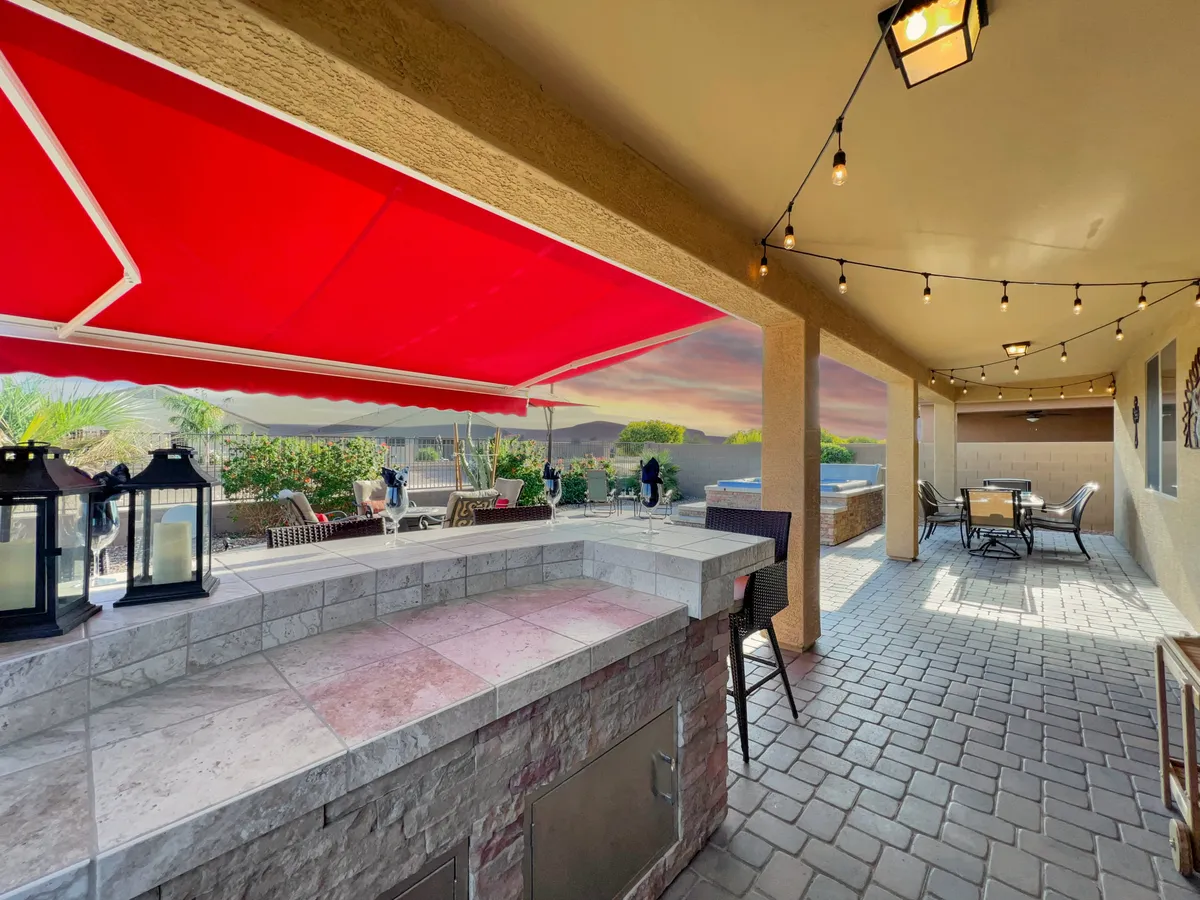 An exterior patio scene with a red awning, outdoor bar, comfortable seating, and a picturesque mountain view in the background. The space is set up for dining, relaxing, and socializing, all while taking in the scenic surroundings.