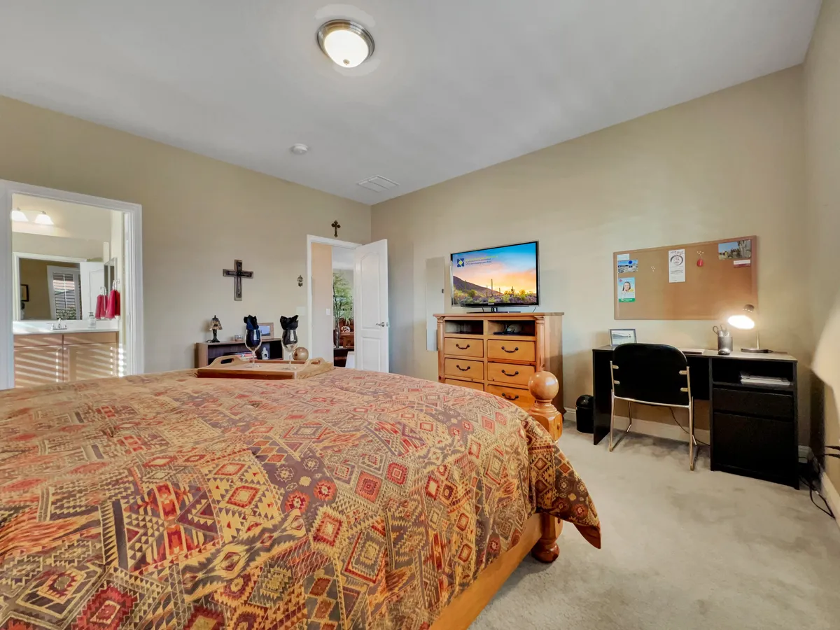 A comfortable bedroom featuring a bed with a patterned cover, a television on a dresser, and a desk with a chair set up for working or studying. The room feels personal and well-lit, providing both a relaxing sleep area and a functional workspace.