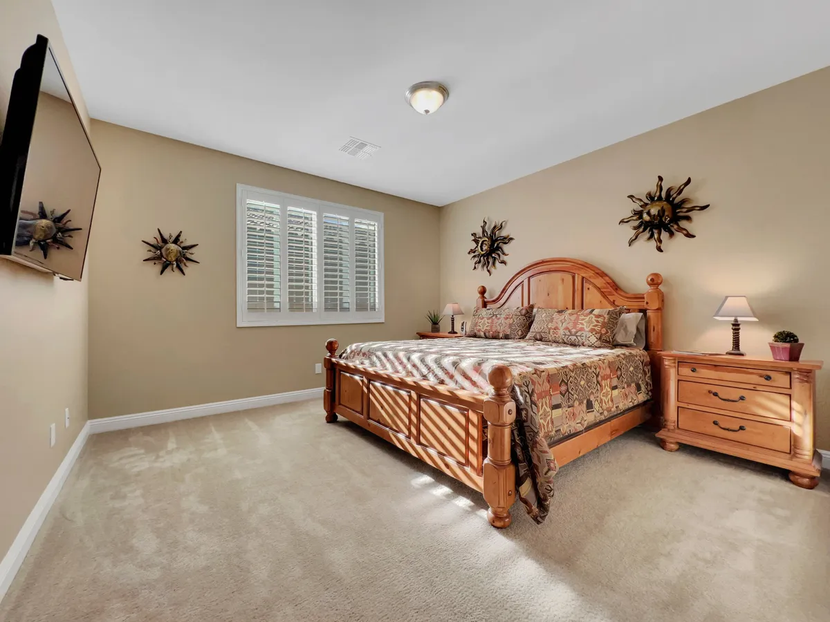 A cozy bedroom featuring a comfortable bed with decorative wall art above, a nightstand with a lamp, and a window letting in natural sunlight. The room exudes warmth and tranquility, suggesting a restful retreat.