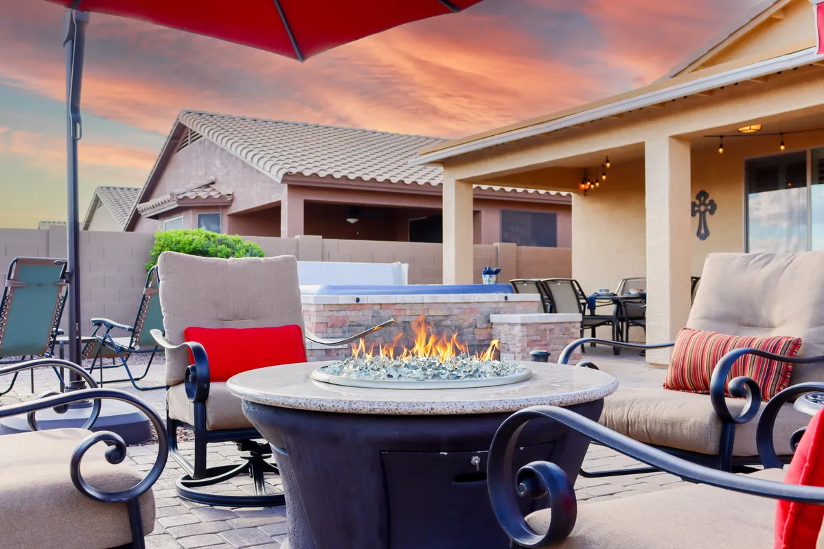A warm exterior scene with a fire pit, comfortable seating, a view of a pool area, and the glow of a sunset sky. The arrangement invites intimate gatherings and leisurely evenings spent outdoors in a luxurious setting.
