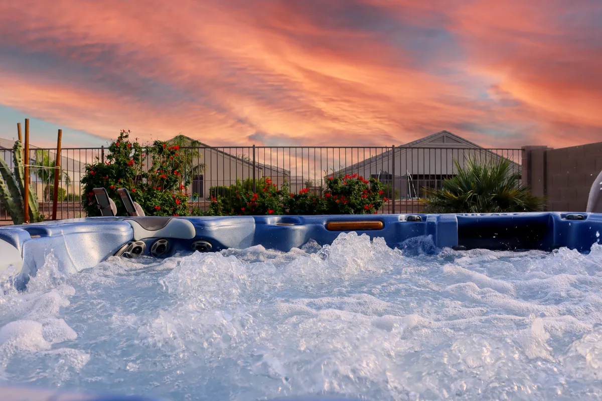 An inviting outdoor hot tub surrounded by lush greenery, with a serene sky overhead. The relaxing spa area is set amidst natural landscaping, perfect for unwinding and enjoying the sunset. This image highlights the luxury and tranquility of private outdoor amenities.