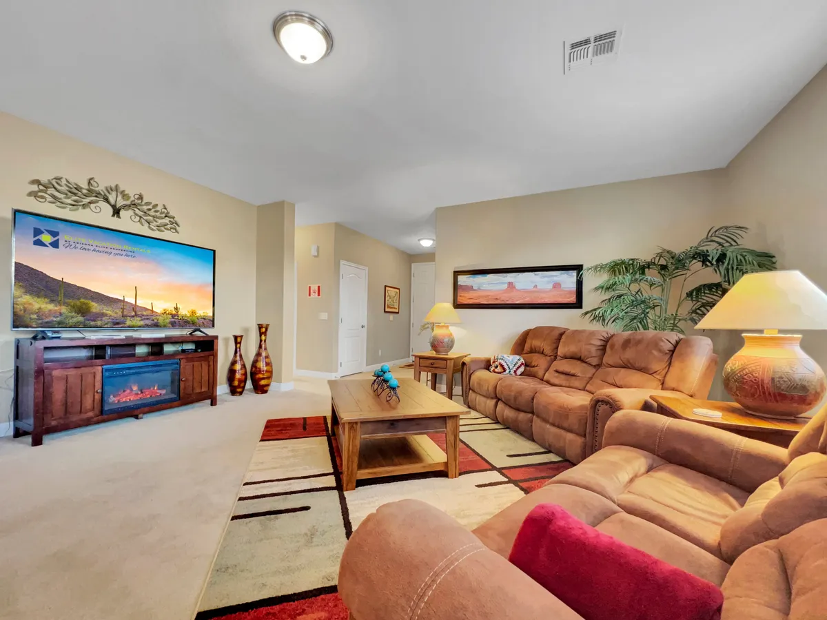 A cozy and comfortable living room scene with reclining sofas, a large TV set against a scenic background, and thoughtful Southwest-inspired decorative accents. The coffee table is styled for gathering and relaxation.