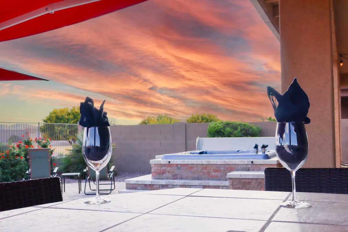 This exterior shot features a luxurious hot tub with elegant glassware and black napkins set nearby, all framed by a stunning, colorful Arizona sunset. The atmosphere is peaceful and romantic, suggesting a perfect setting to unwind and soak in the desert ambiance.