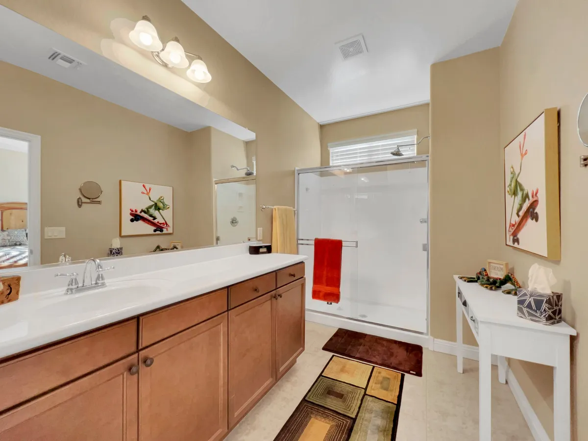 A bright en-suite bathroom with a double sink vanity, glass shower enclosure, and colorful towels. Artwork on the wall and natural light enhance the spa-like atmosphere, creating a sense of luxury and calm.